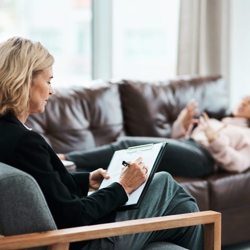 Shot of a mature psychologist writing notes during a therapeutic session with her patient